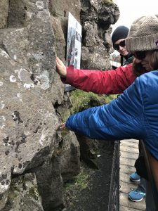 Photo of Amy on a boardwalk that is descending between two rock walls, which are the edges of the North American and Eurasian Plates. She is reaching out at touching a rock wall.