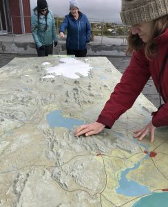 Photo of Amy touching the elevation map of southwest Iceland. Hilary and Alison are standing at the far end of the large outdoor table map