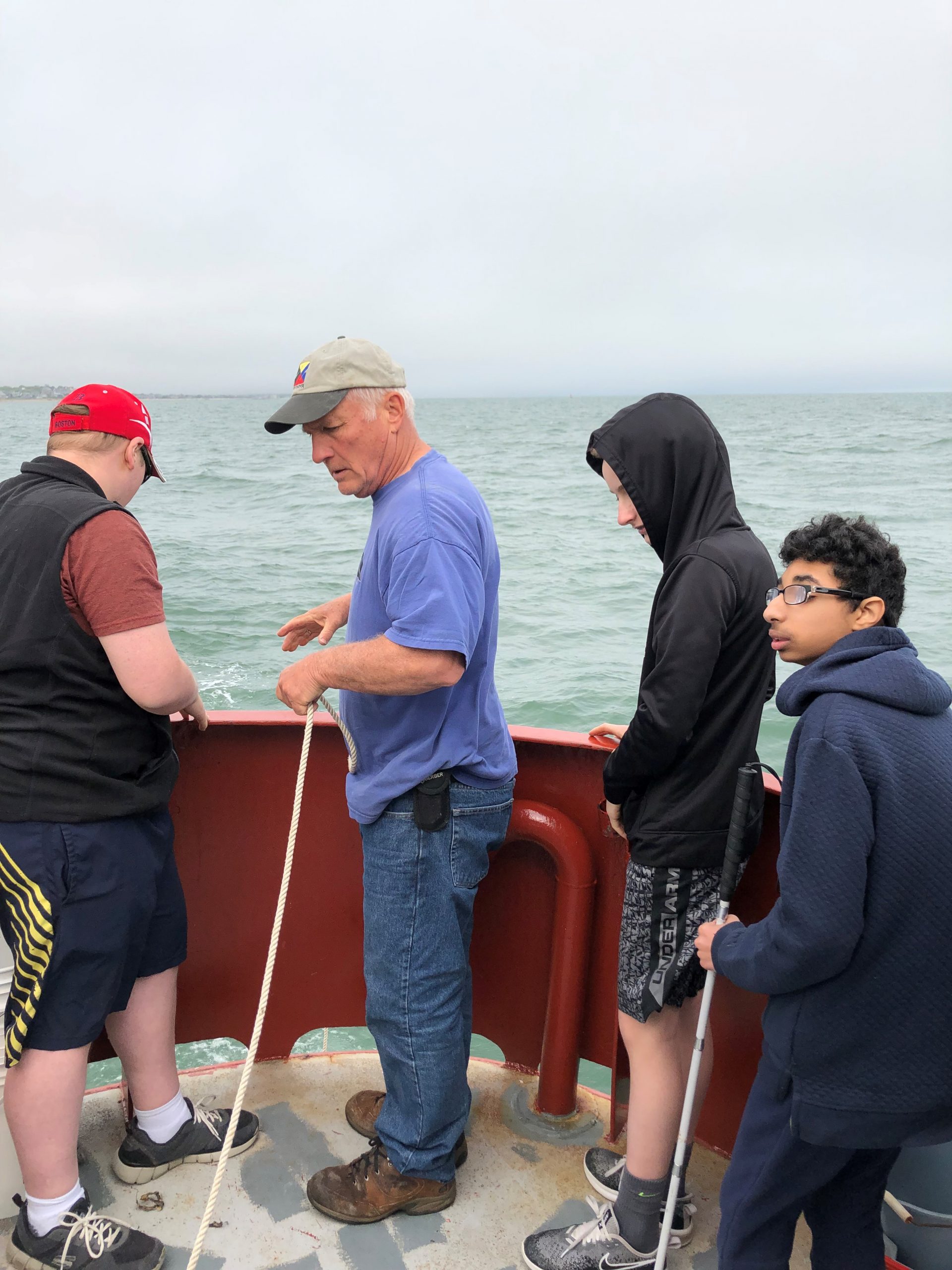 A photo of Rob Reynold,s the educator on our boat trip, and three students work to lower a dredge over the railing of our chartered boat.